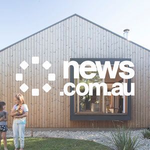 A woman and a child are standing in front of a wooden house.