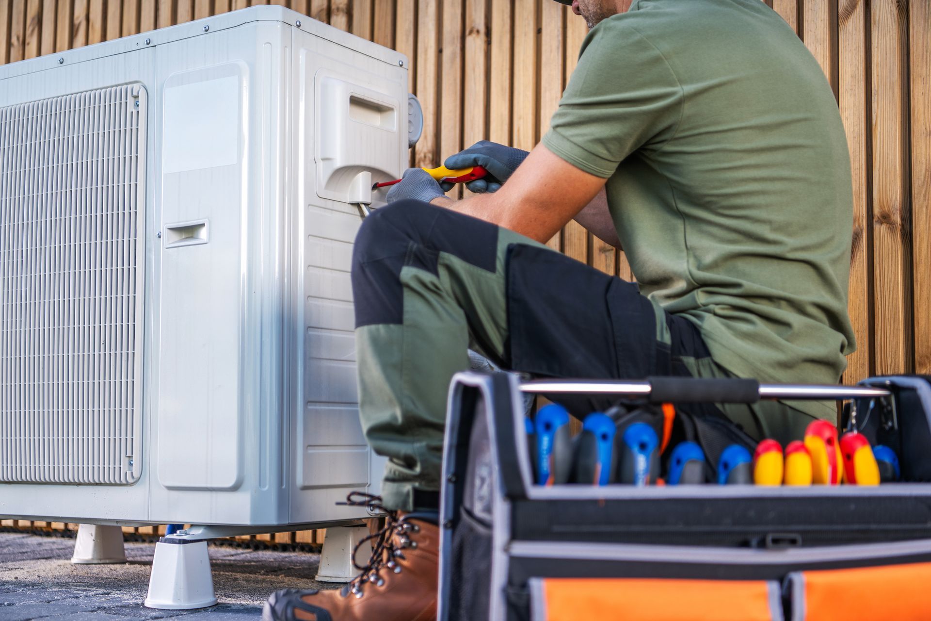 Technician servicing outdoor HVAC unit with toolbox beside him. Technician servicing outdoor HVAC unit with toolbox beside him.
