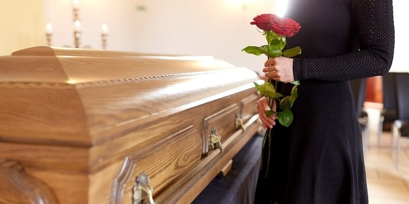 a woman is holding a rose in front of a casket at a funeral .