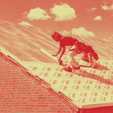 Two workers on a rooftop installing material; one crouches, the other stands. Sunlight illuminates the scene.