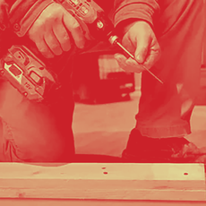 A person, kneeling, uses a screwdriver to work on a wooden structure indoors.