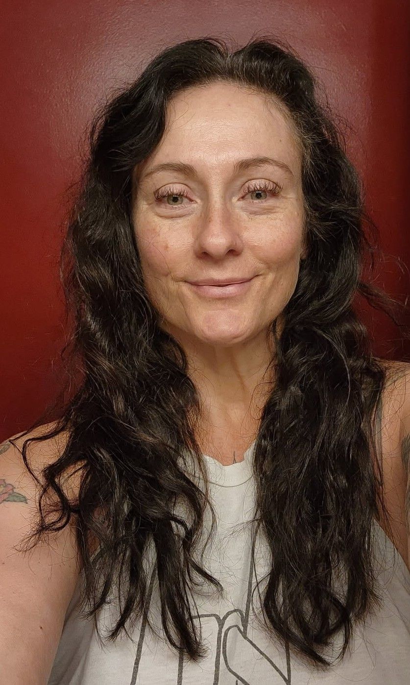 Man with beard smiling, wearing black t-shirt with American flag mustache design against yellow wall.