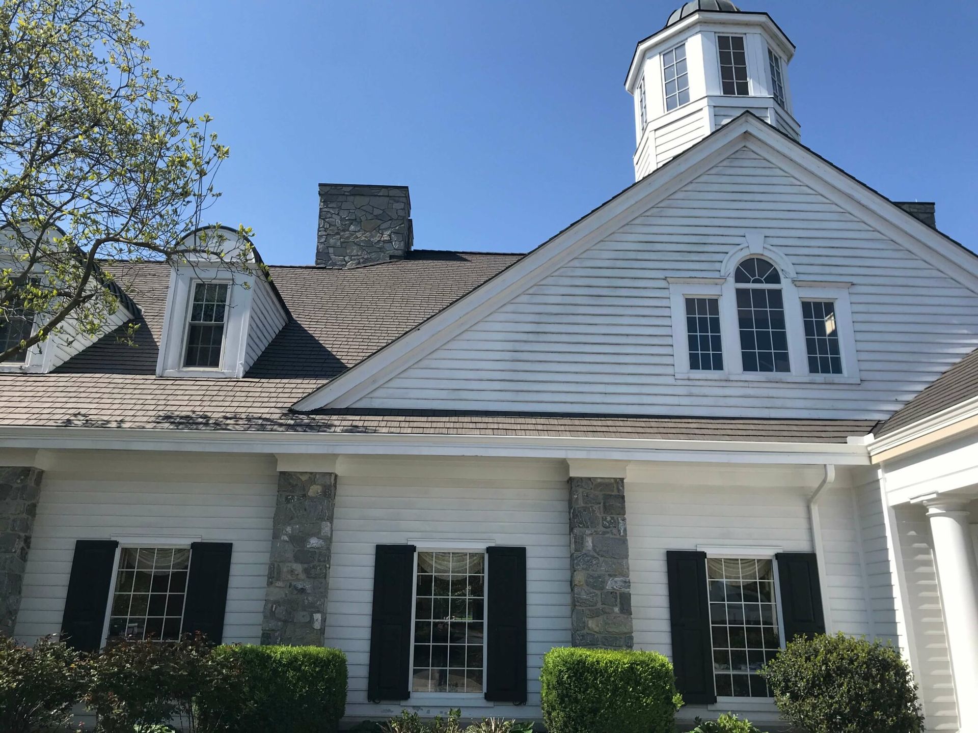 White building with a cupola, dormers, stone accents, and black shutters. Sunny day with clear blue sky.