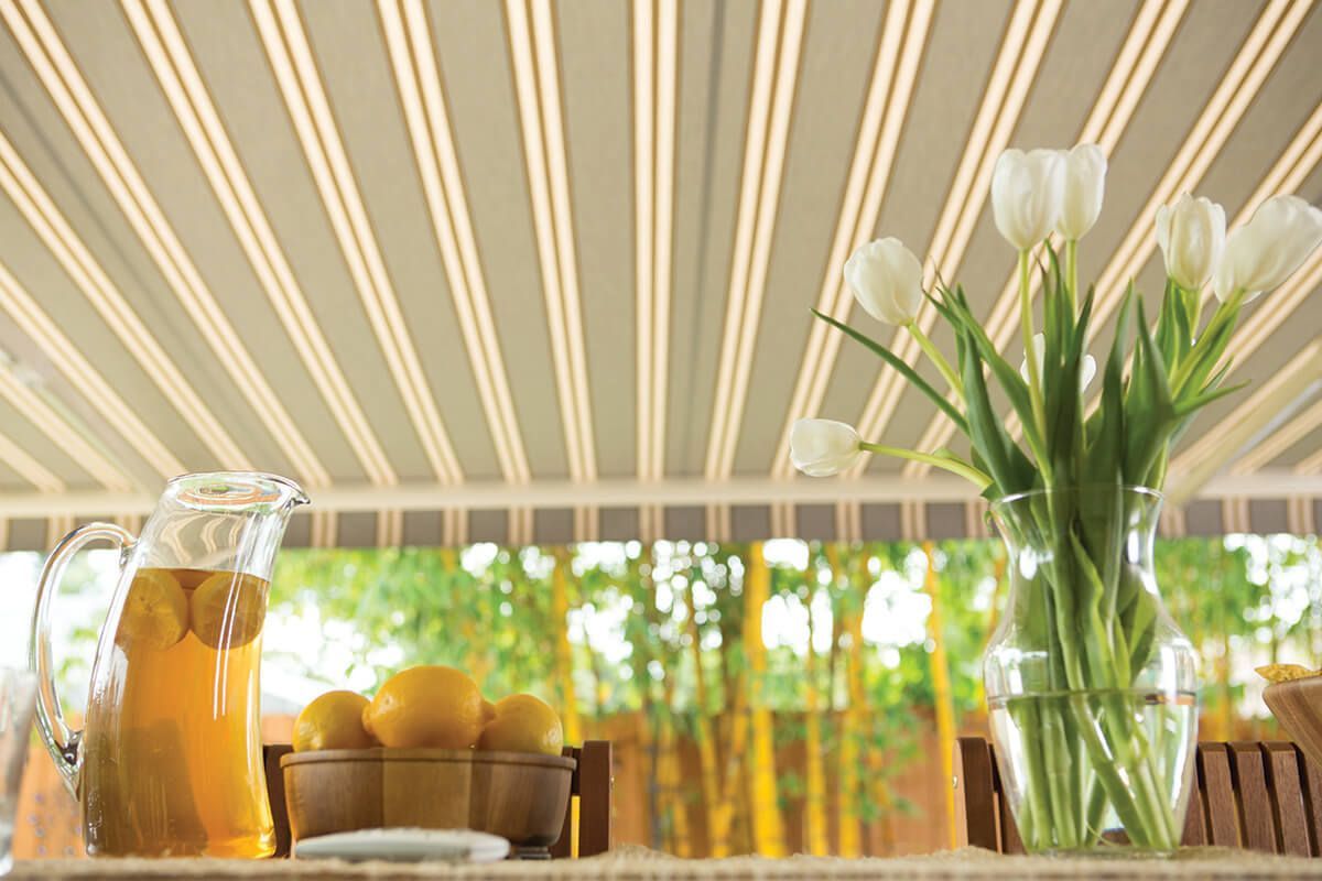 A pitcher of lemonade, lemons, and white tulips on a table under a striped awning.