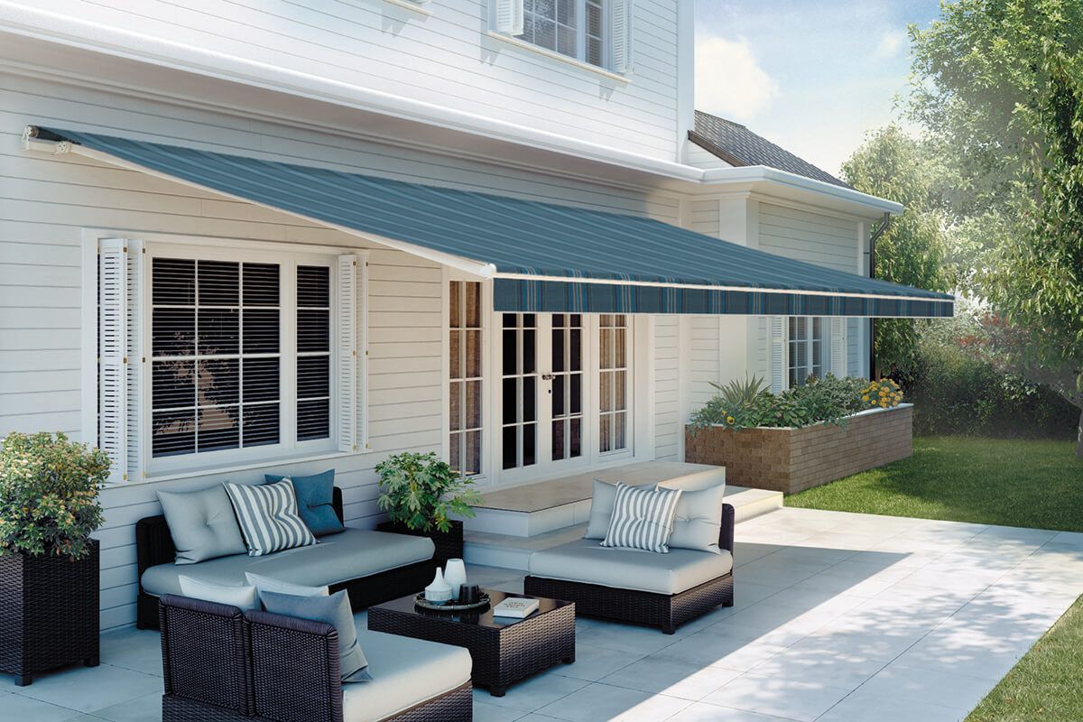 A patio with outdoor furniture, under a blue awning, next to a white house.