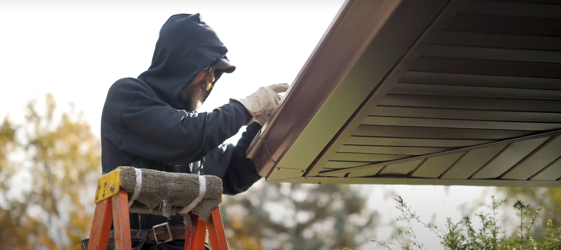 Century Home Improvements - A person in a hooded sweatshirt on a ladder repairs an gutter.