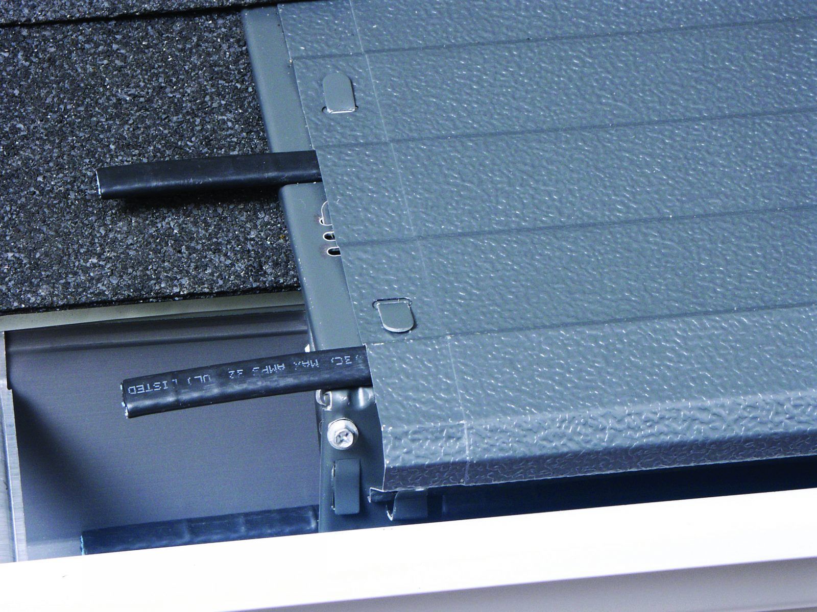Gray gutter guard installed under roof shingles, protecting the gutter from debris.