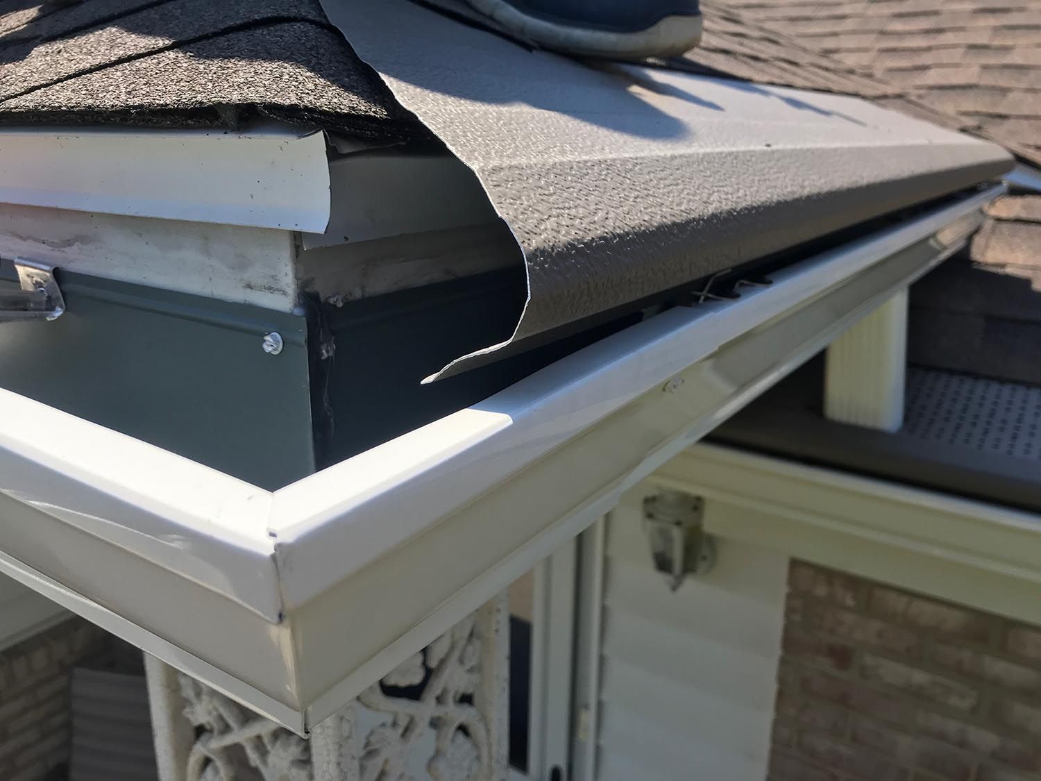 Close-up of a house gutter with damaged roofing material, likely from wind or weather.