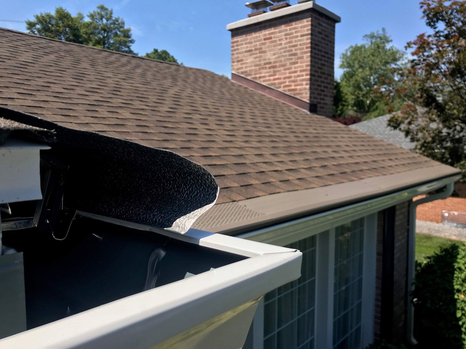 Gutter guard installed on a house with a brown shingle roof, white gutters, and a brick chimney.