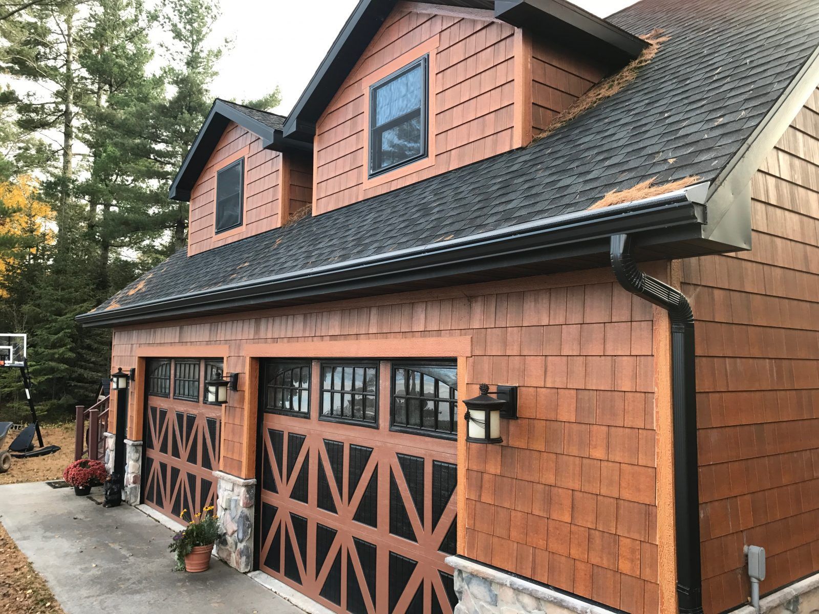 Two-story garage with brown wood siding, black roof, and matching garage doors; a concrete driveway is in front.