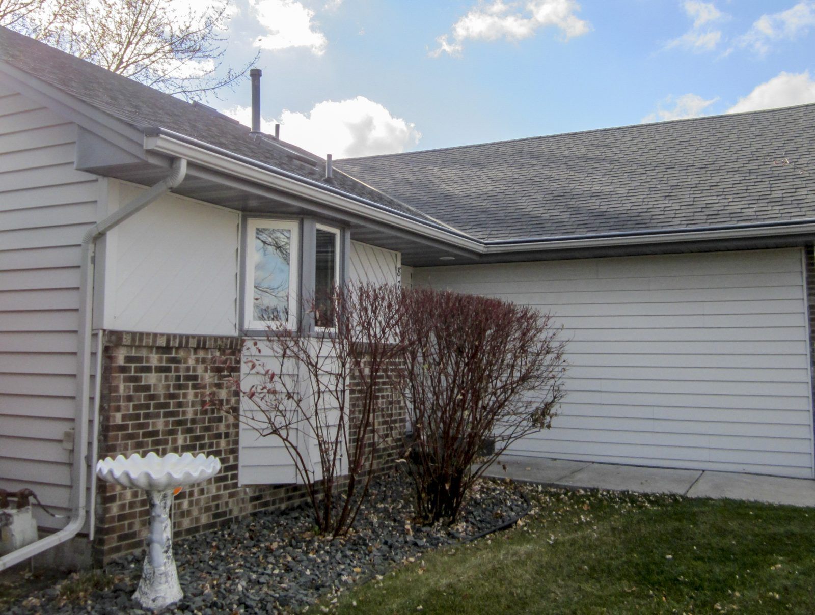 Corner of a house with white siding, brick, and gray shingles. A birdbath is on the left.