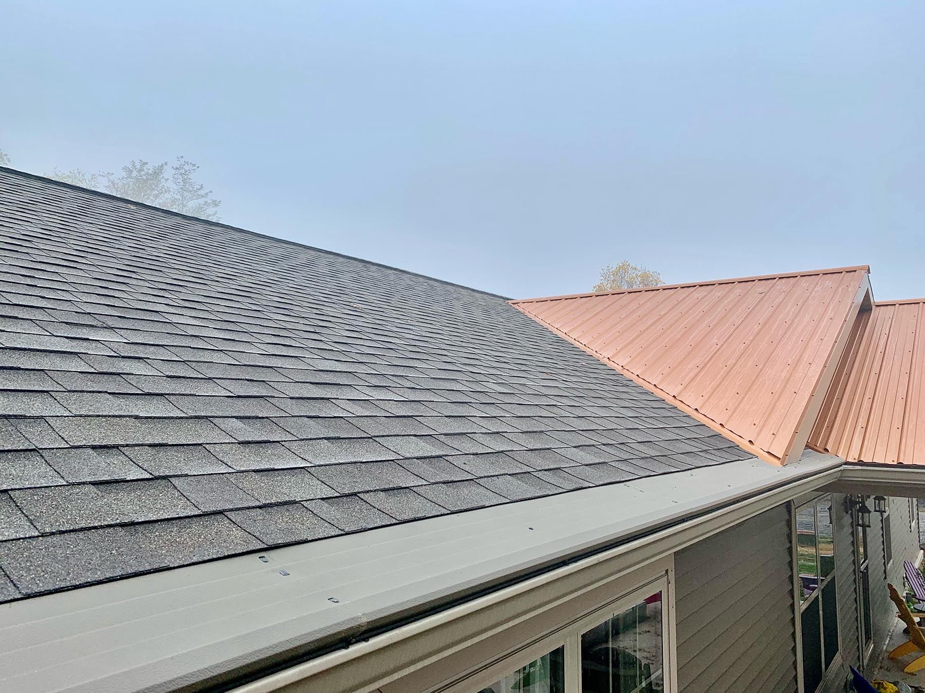 Gray shingle roof and copper-colored metal roof section on a house, with a gutter along the edge.