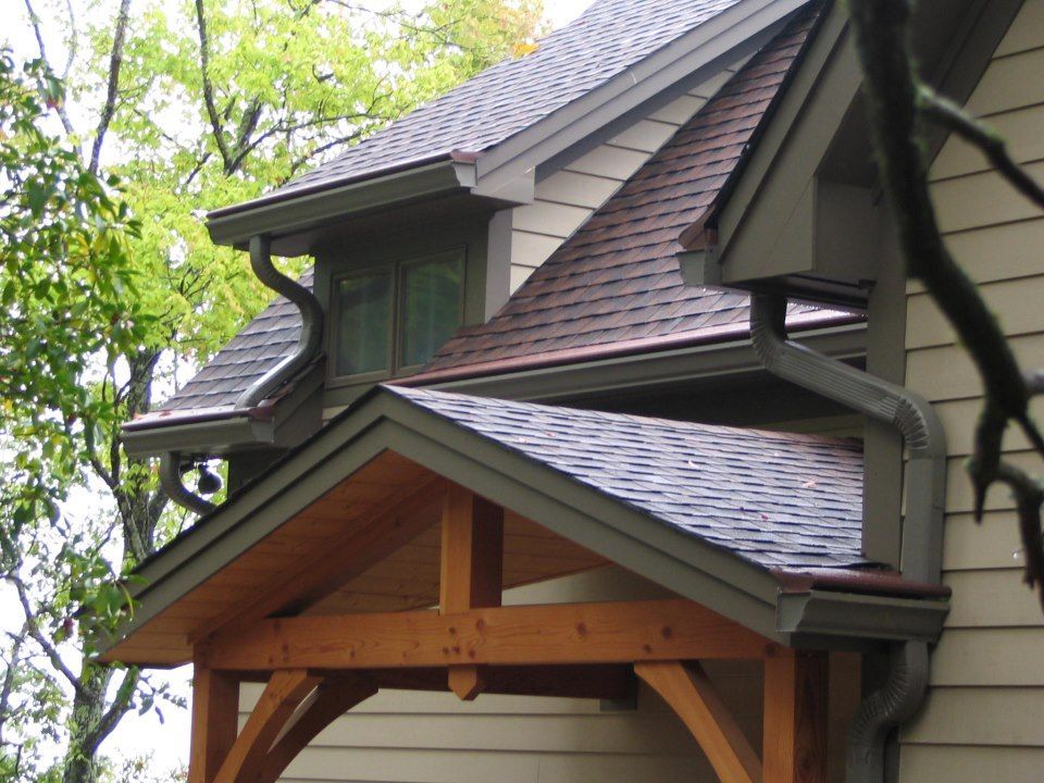 Brown shingled roof with copper gutters and a wooden porch overhang on a house.