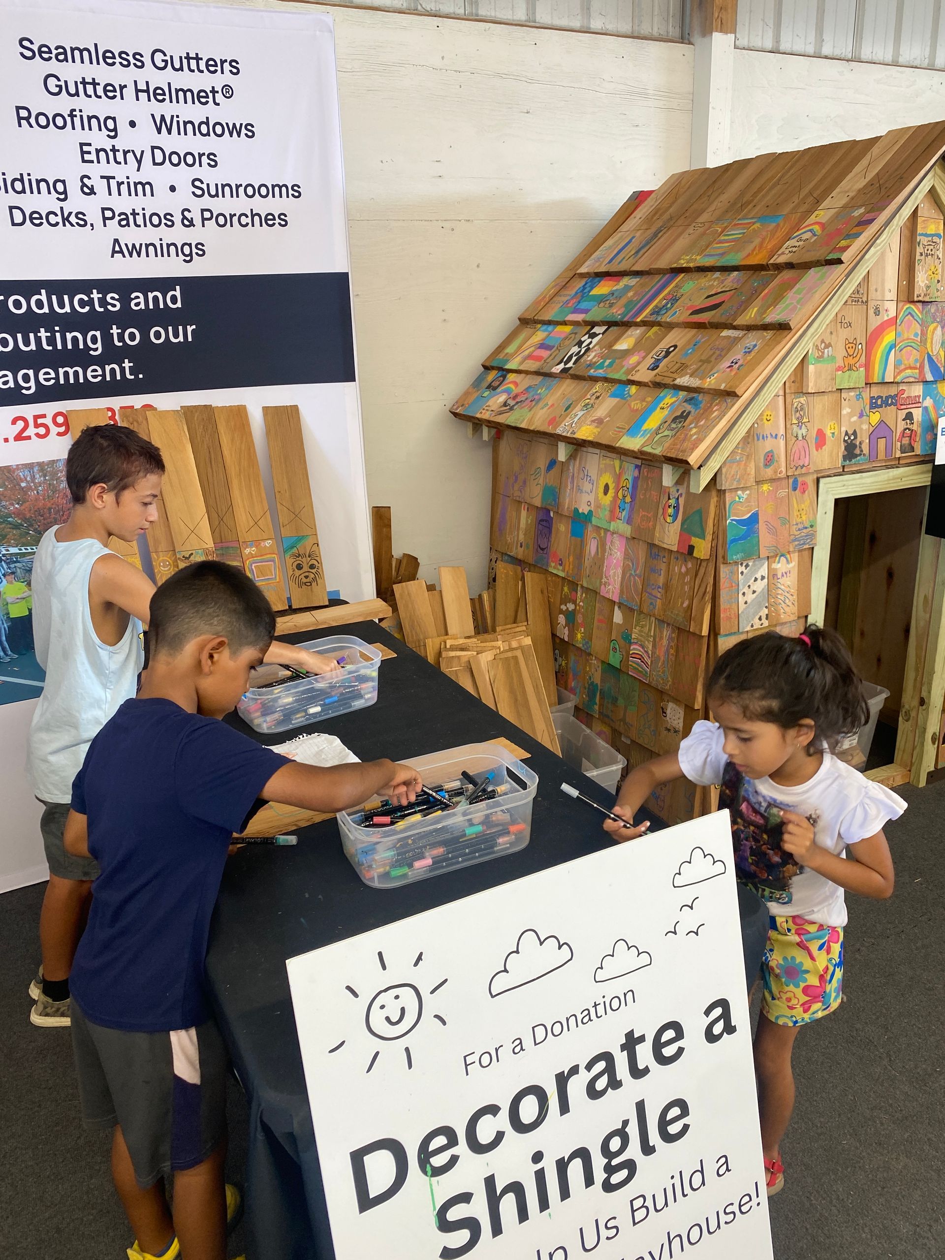 Century Home Improvements - Community Involvement - Children decorate shingles at a booth with a wooden house.