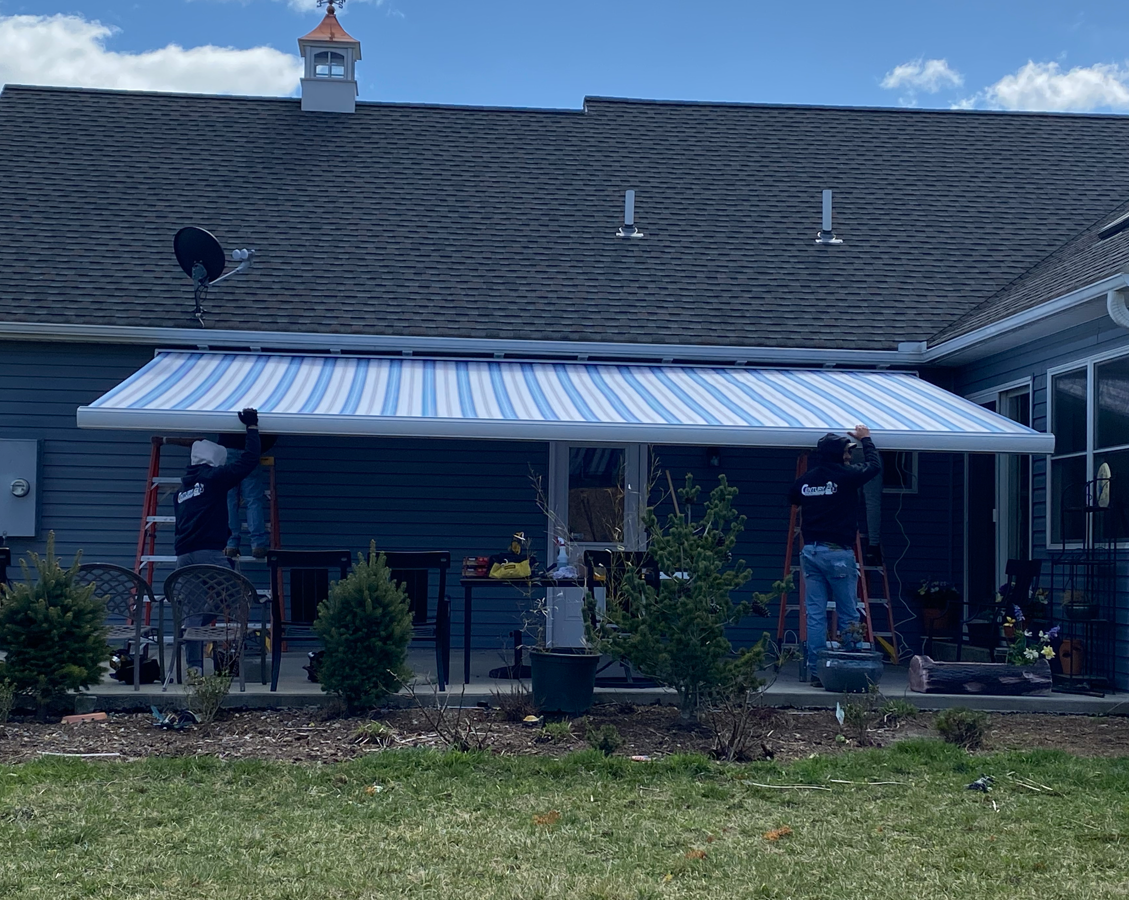 Workers installing a blue and white striped awning on a house, sunny day.