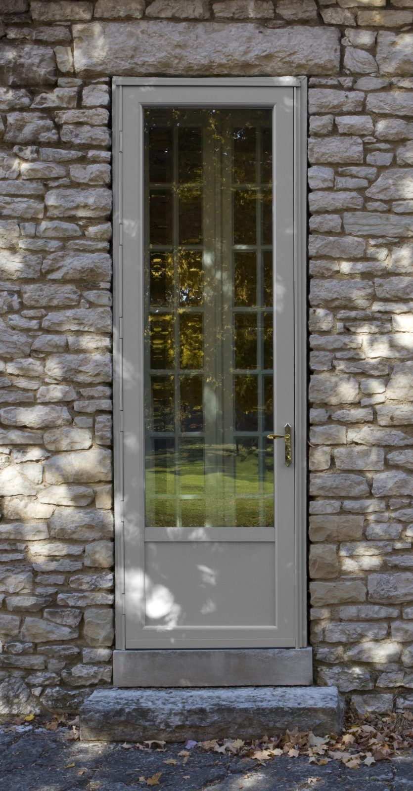 A narrow, pale gray door with a glass window framed by stone brick.