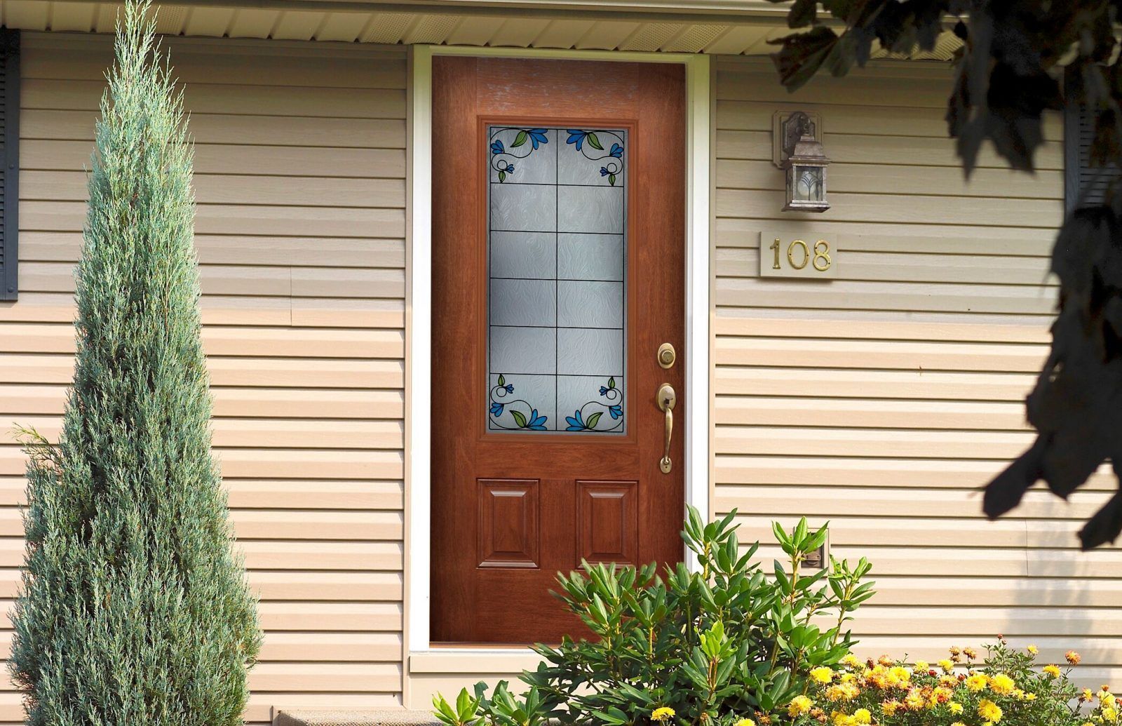 Brown front door with glass panel decorated with blue and green vines, set in a beige-sided house, number 109 above the door.