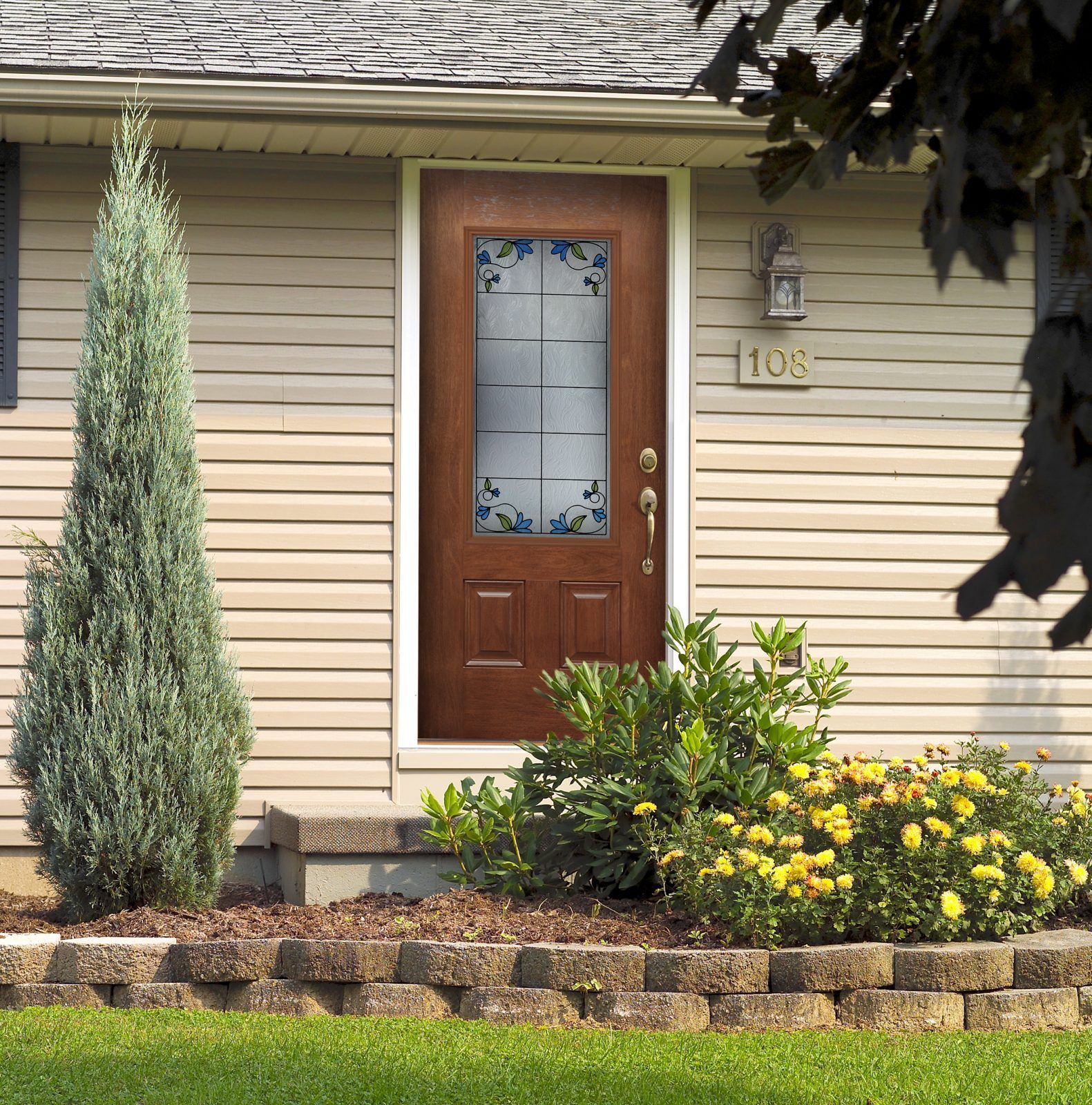 A brown front door with a glass window, flanked by landscaping, on a beige house.