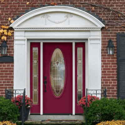 Red front door with oval glass and sidelights, white trim, and arched pediment on a brick house.