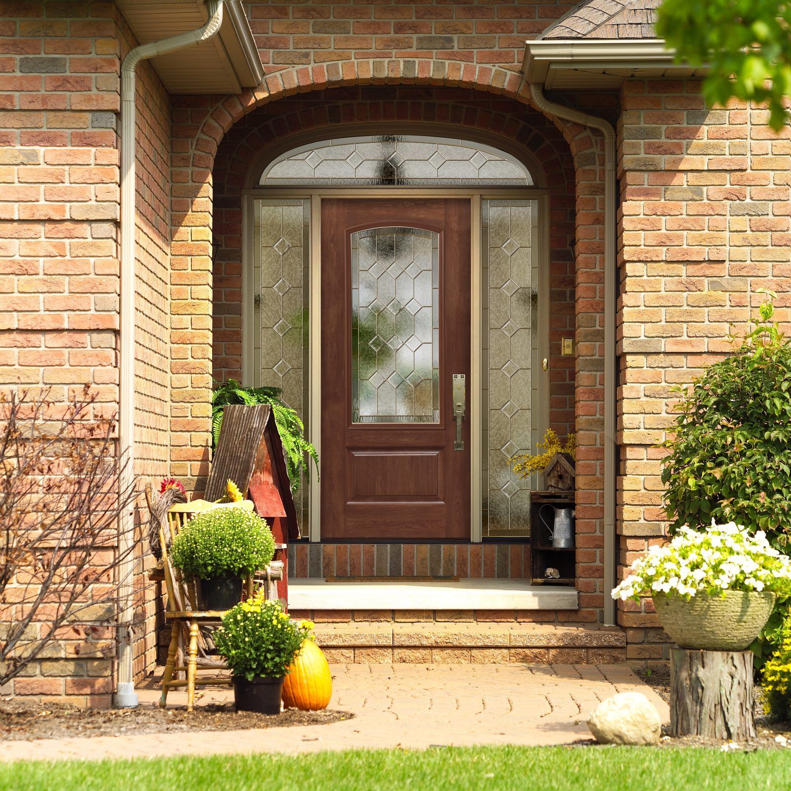 Brick home entrance with a brown door, sidelights, and a semi-circular window. 