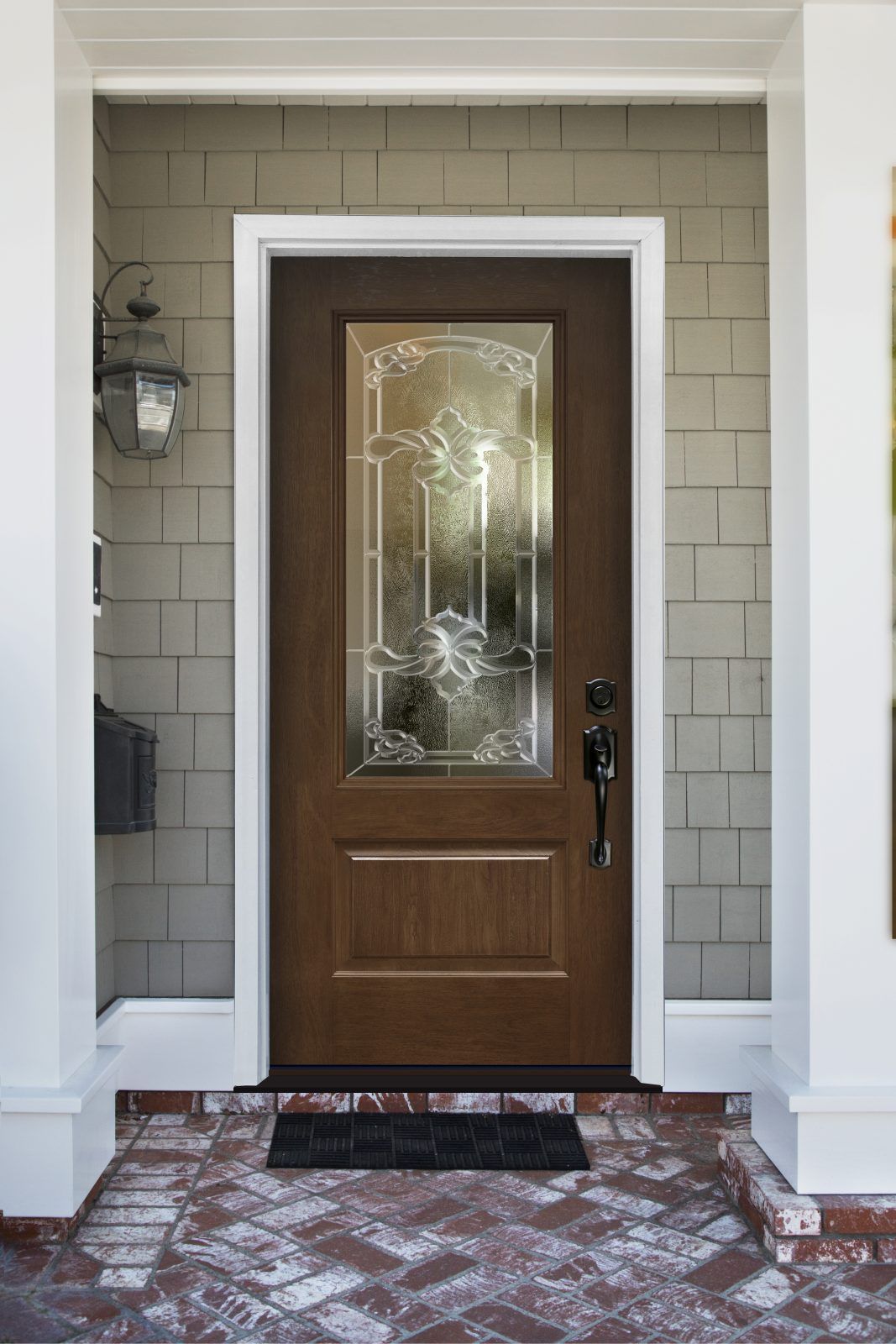 Brown front door with glass panel, set in white frame, brick porch, and gray siding.