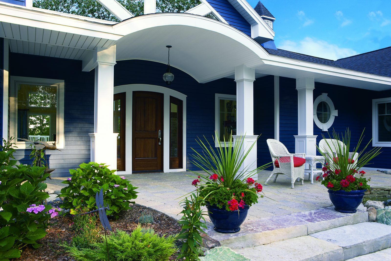 Blue house with white trim, porch with chairs, and flower pots.