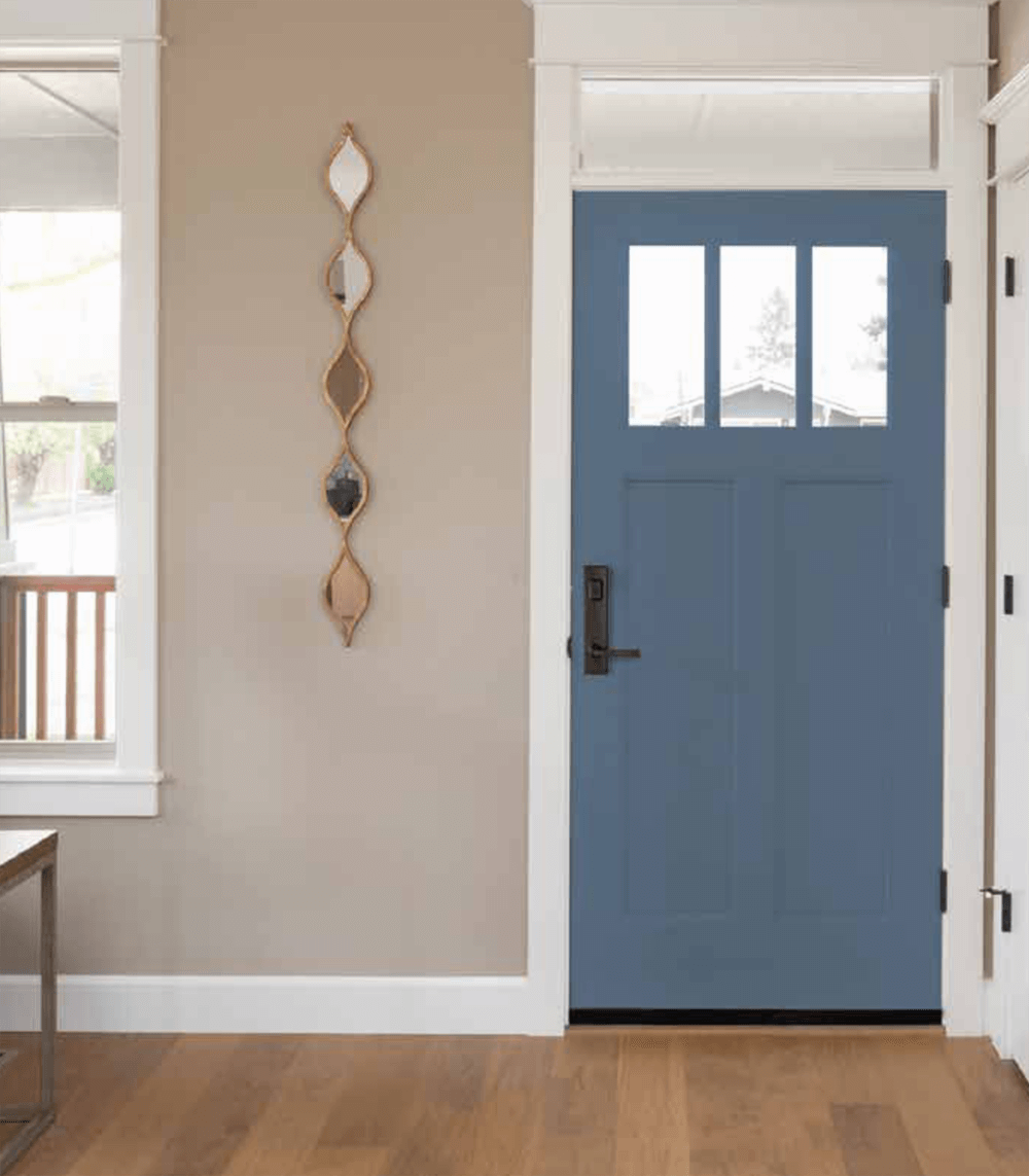 Blue front door with glass panes and black hardware, tan wall, and gold-framed decorative mirrors.
