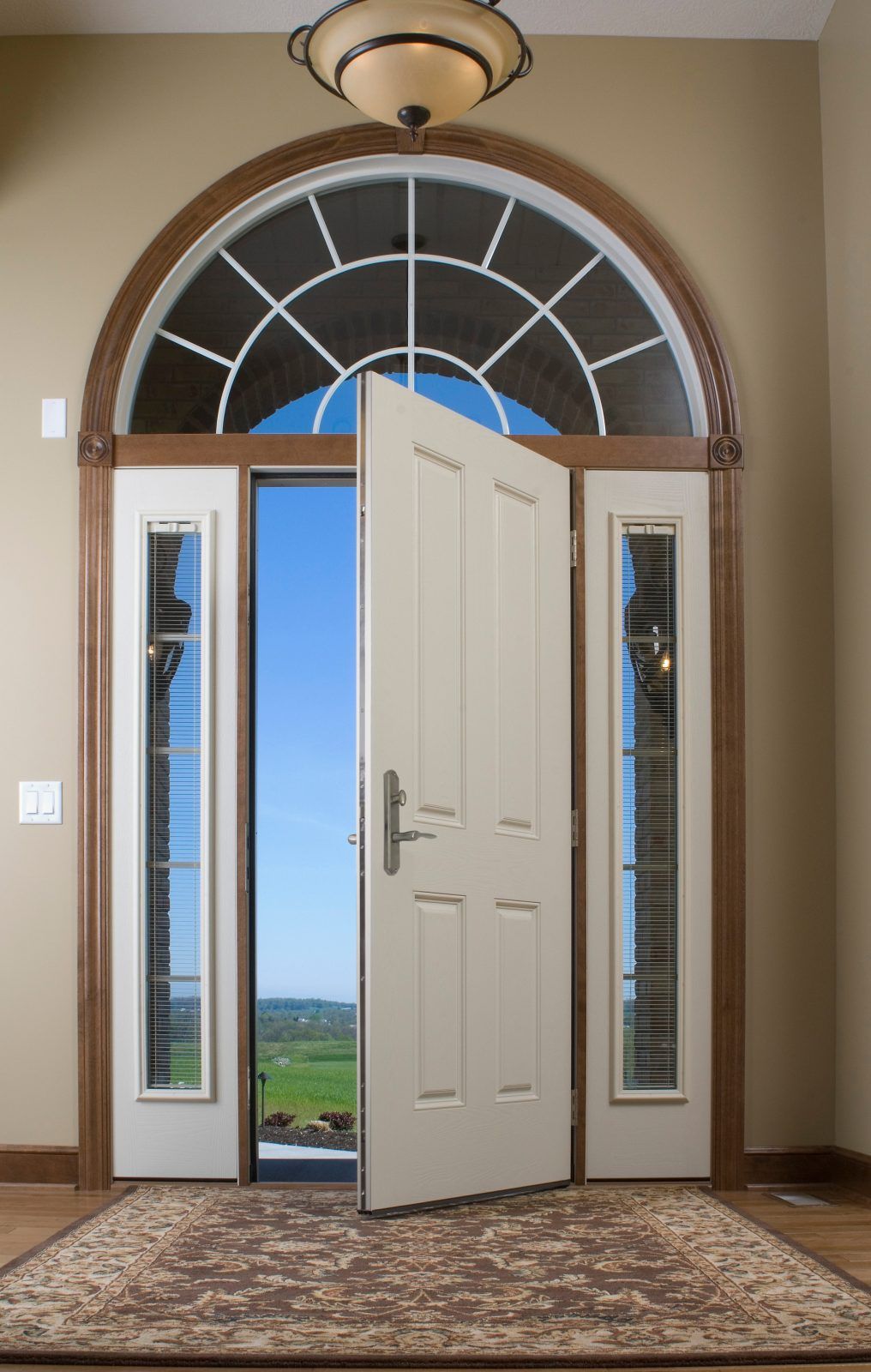 Beige front door, ajar, revealing a bright blue sky and landscape.