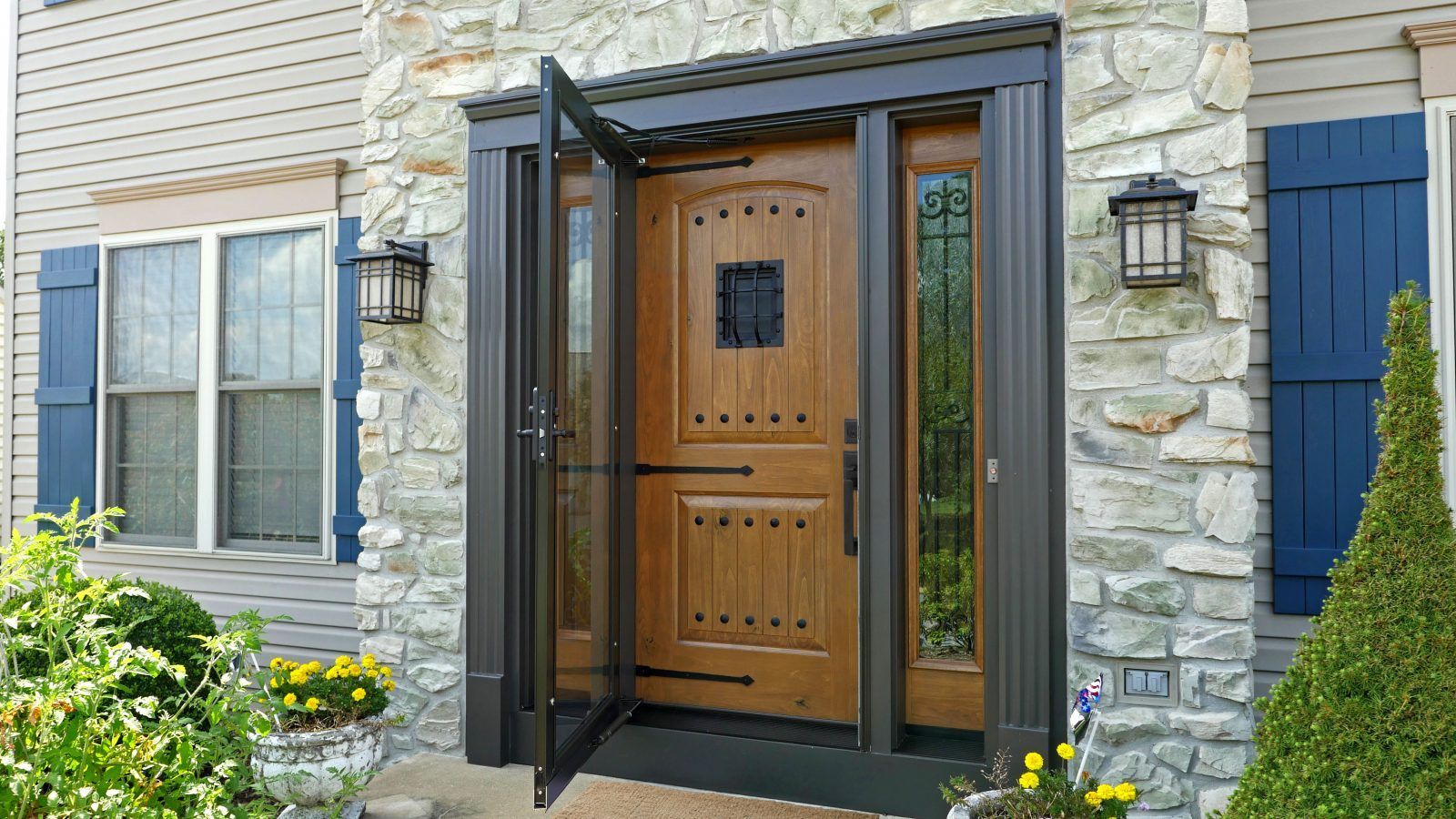 Wooden front door with a glass storm door and sidelights, surrounded by stone siding.