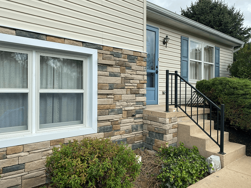House exterior with stone veneer and cream siding, blue door, and black handrail.
