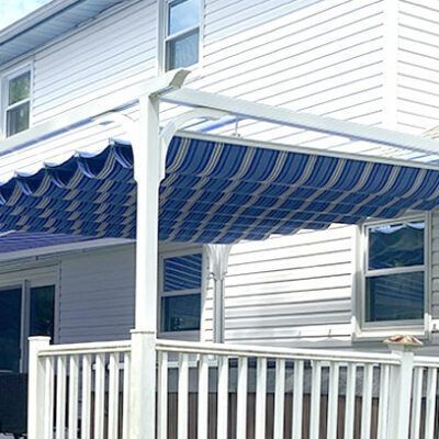 Blue and white striped awning on a white pergola over a deck, attached to a white house with windows.