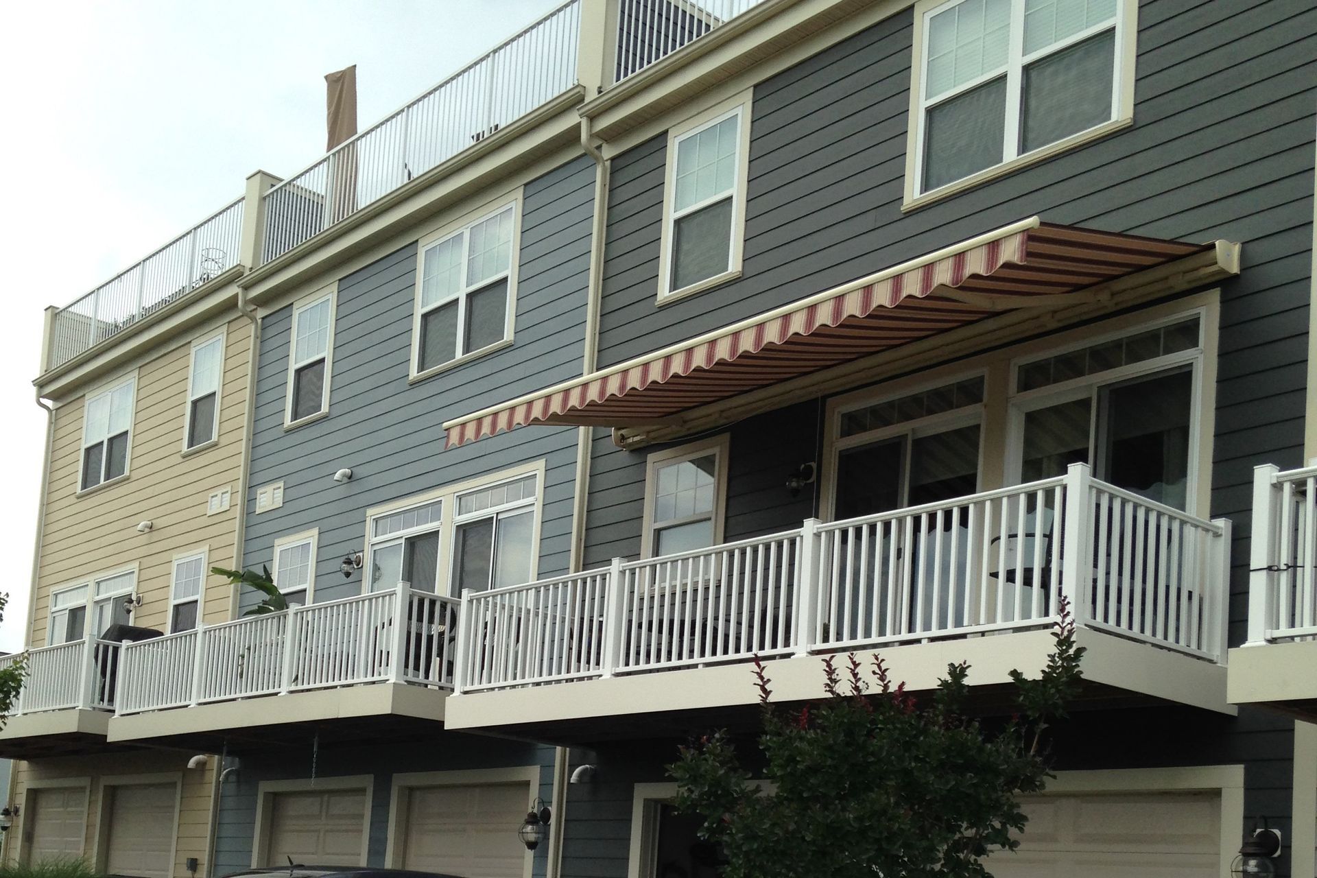 Row of townhouses with decks, awnings, and garage doors. Gray and beige siding.