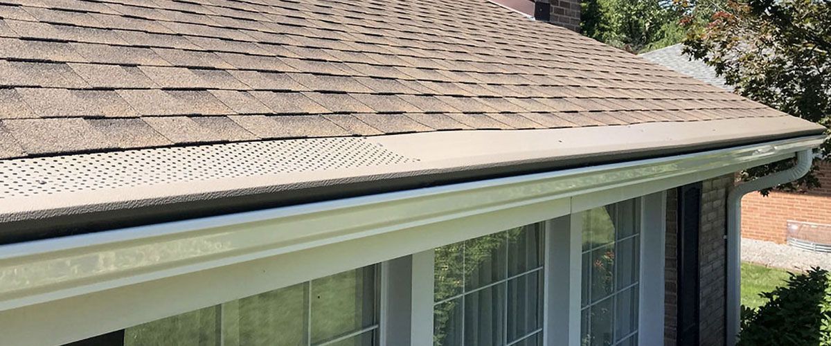 A close-up of a house roof with shingles and a white gutter along the edge.