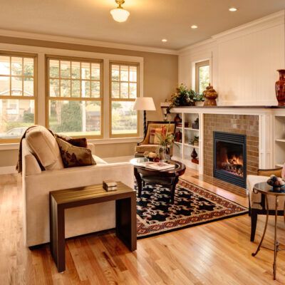 Cozy living room with fireplace, couch, windows, and hardwood floors. Creamy walls and trim with neutral-toned furniture.