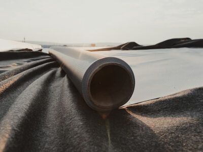 A dark gray rolled tube lying on a dark fabric, with a blurred background.