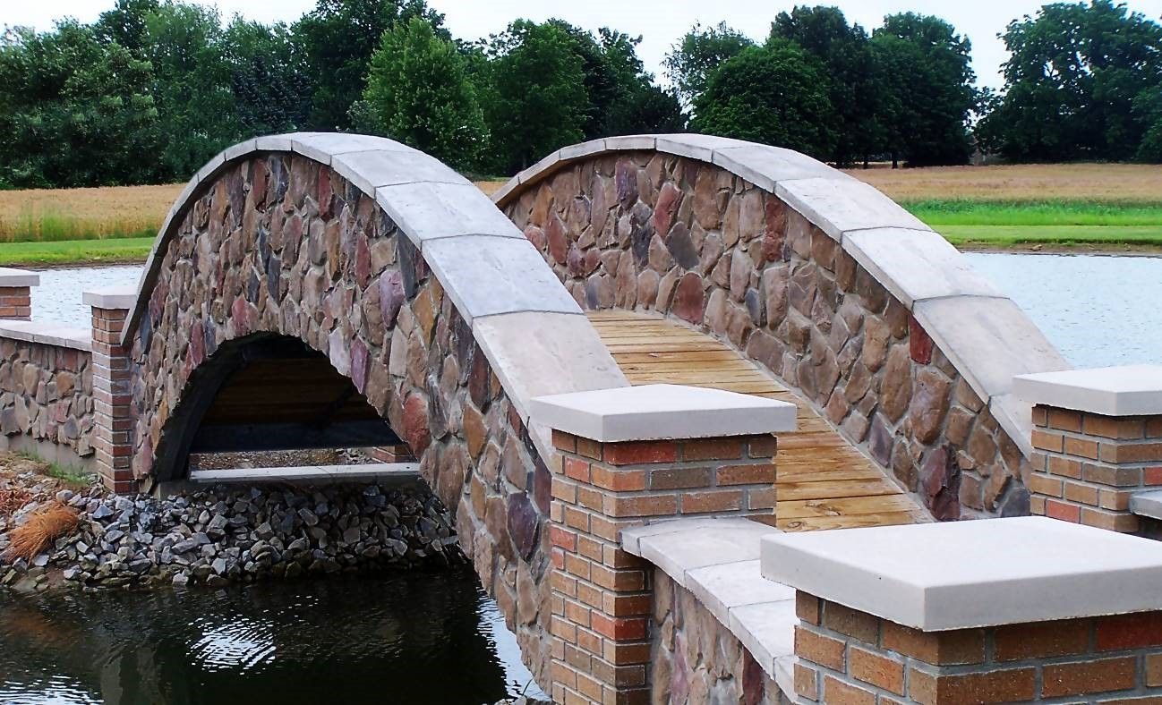 Stone arch bridge over water, with a brick and stone facade; trees in the background.