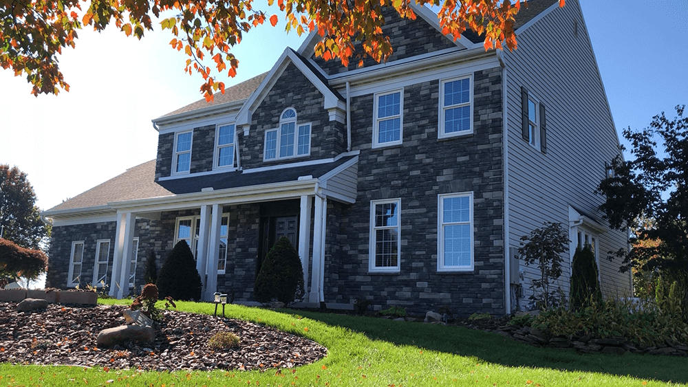 Two-story house with stone facade, white trim, and a green lawn under a sunny sky.