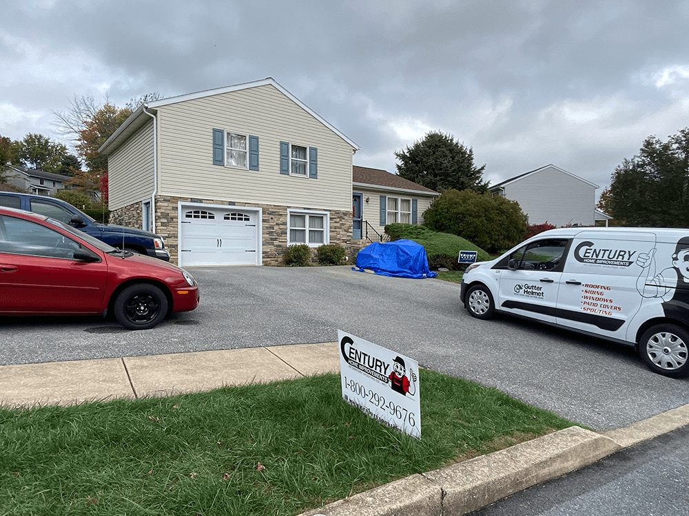 A two-story house with a driveway. A red car and a white van are parked in the driveway. A sign on the lawn.