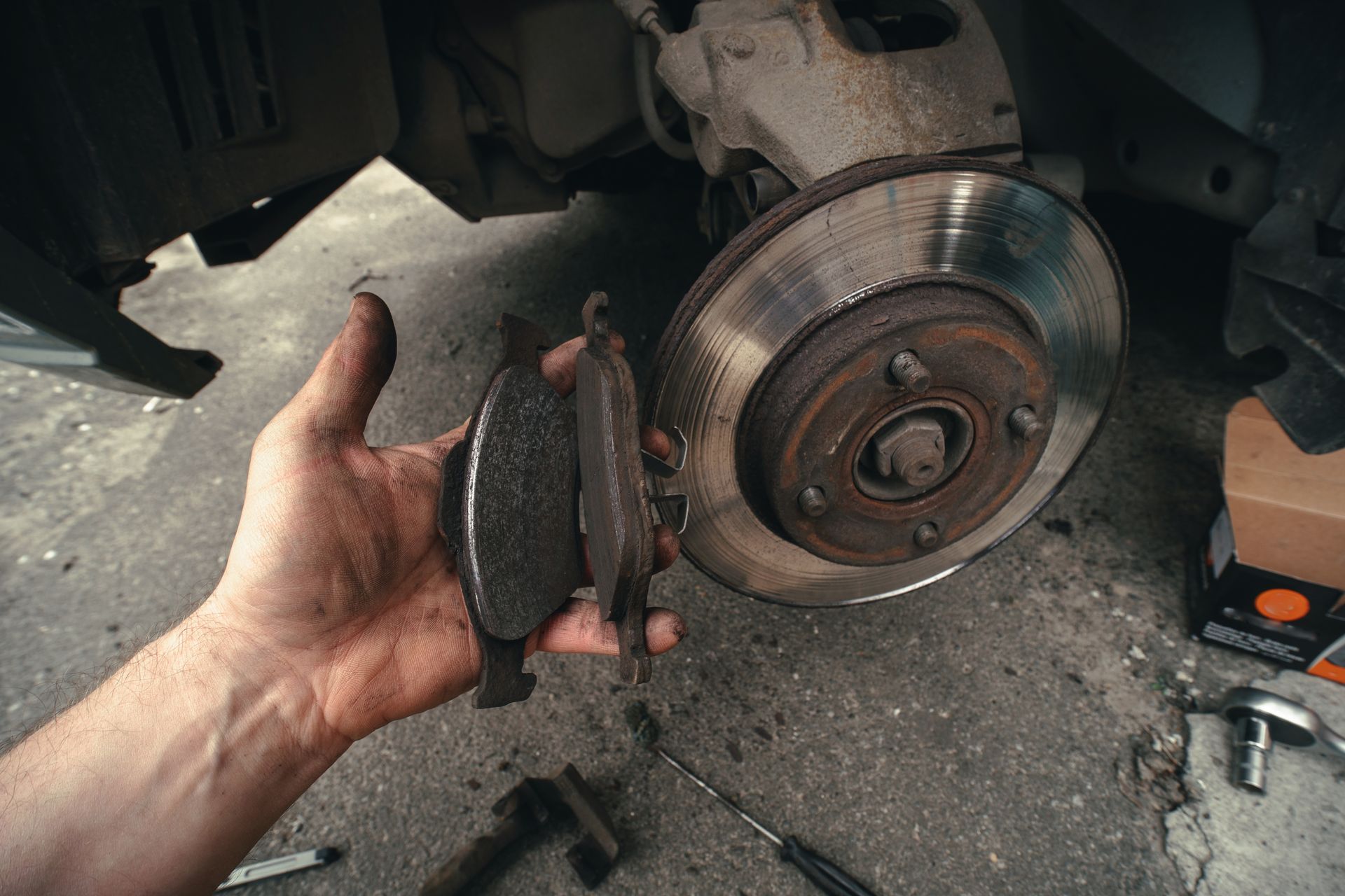 A person is holding a pair of brake pads in front of a car  | Corb's Auto Repair LLC