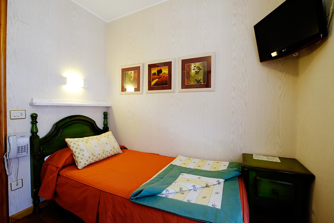 Pequeña habitación de hotel con una cama individual, TV y obras de arte en la pared.