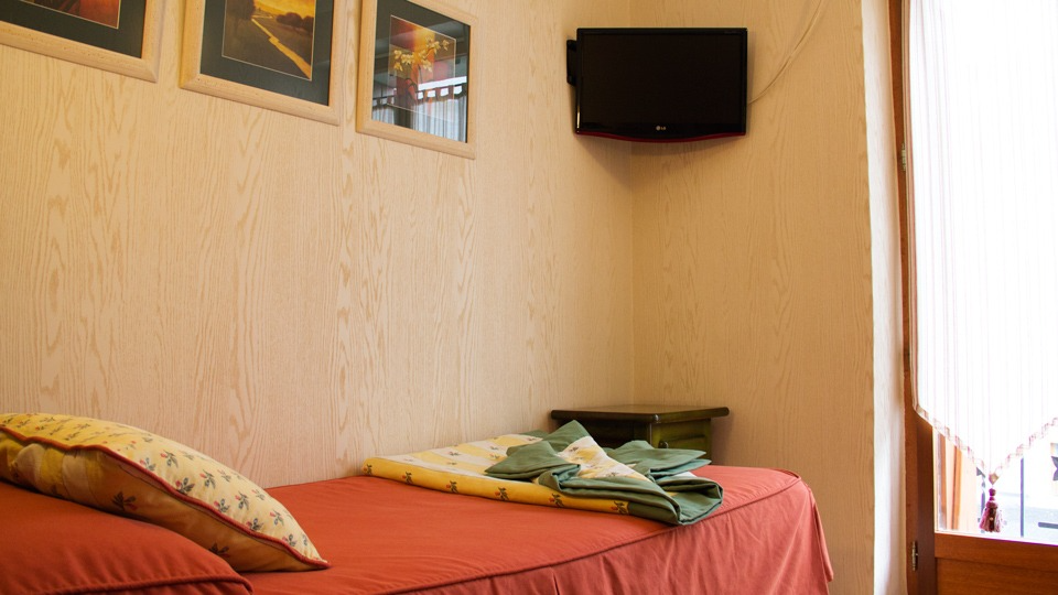 Una pequeña habitación de hotel con una cama individual, un televisor y obras de arte en la pared.