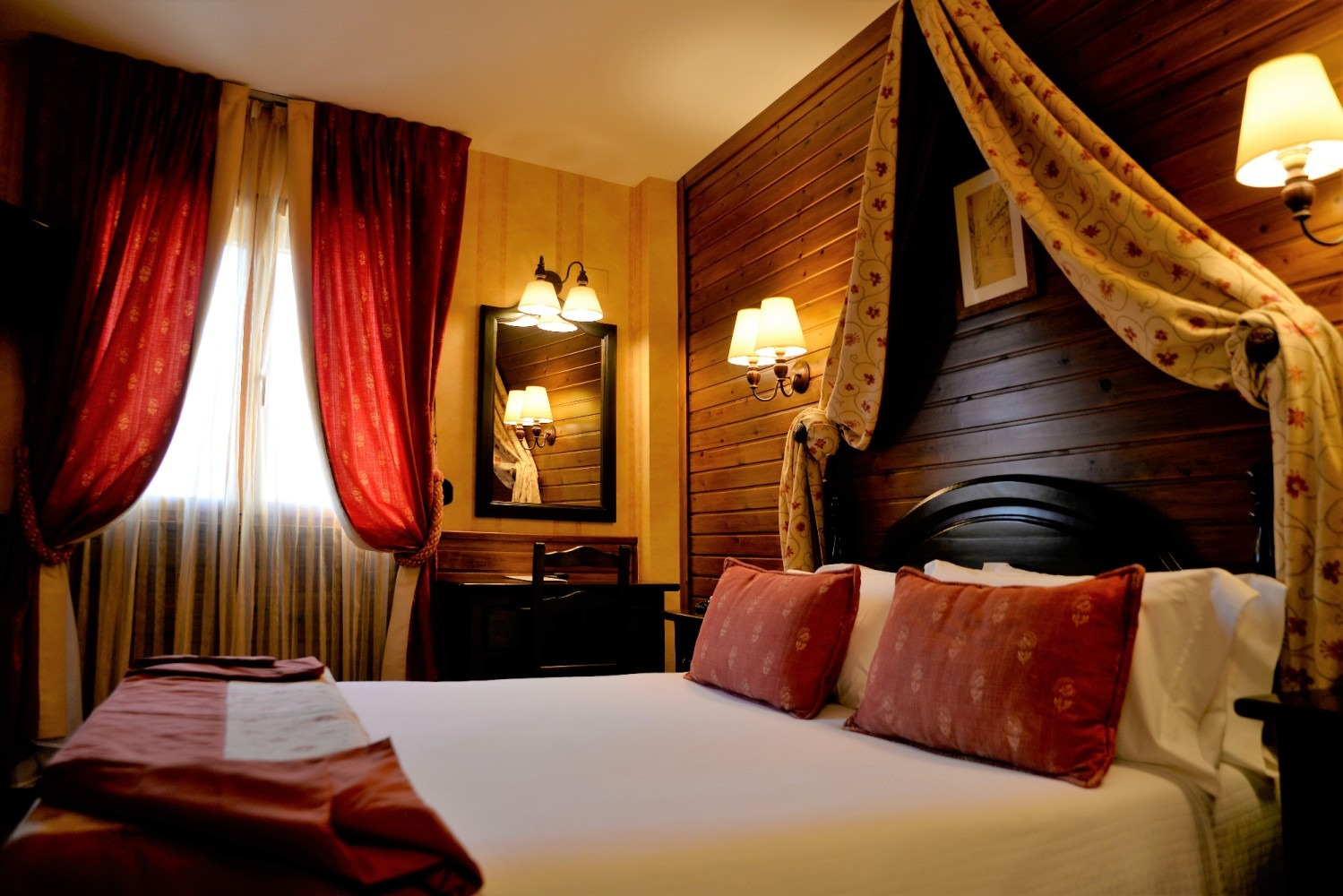 Dormitorio con cama con dosel, cortinas rojas y doradas y paneles de madera oscura.