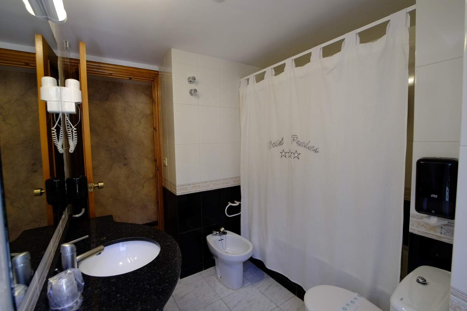 Baño con azulejos en blanco y negro, lavabo, inodoro y cortina de ducha.