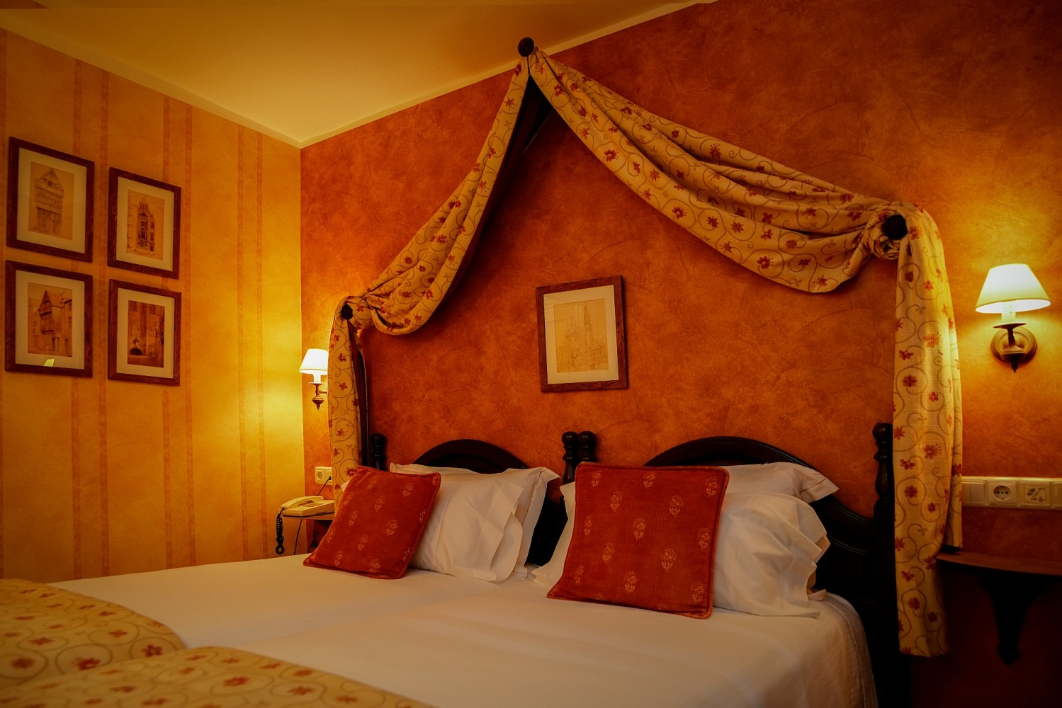 Una cálida habitación de hotel con una cama con dosel, paredes naranjas y obras de arte decorativas.