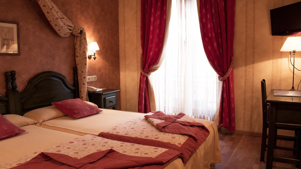 Dormitorio de hotel con dos camas, cortinas rojas y escritorio.