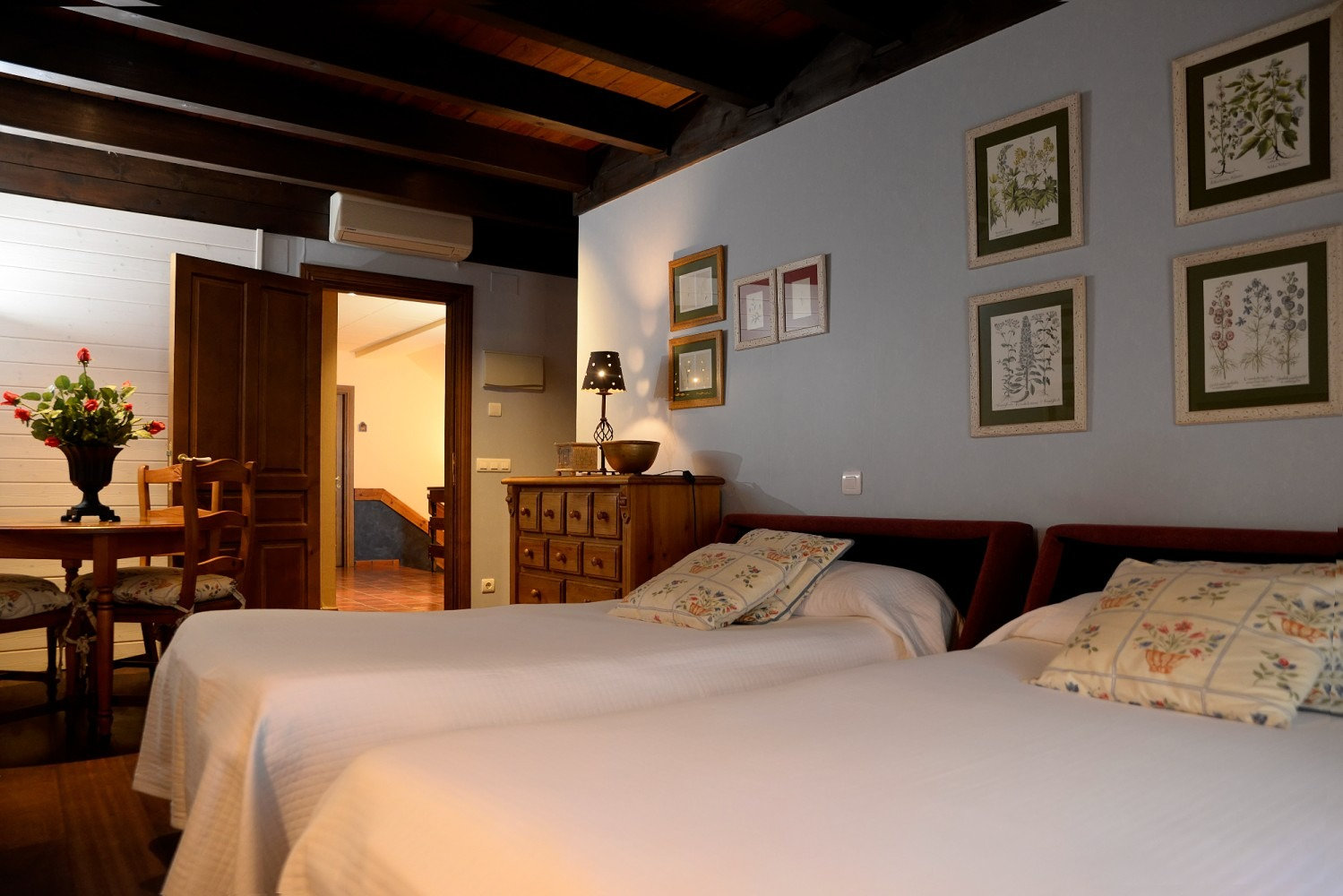 Dormitorio con dos camas individuales, paredes azules, muebles de madera y láminas botánicas enmarcadas.