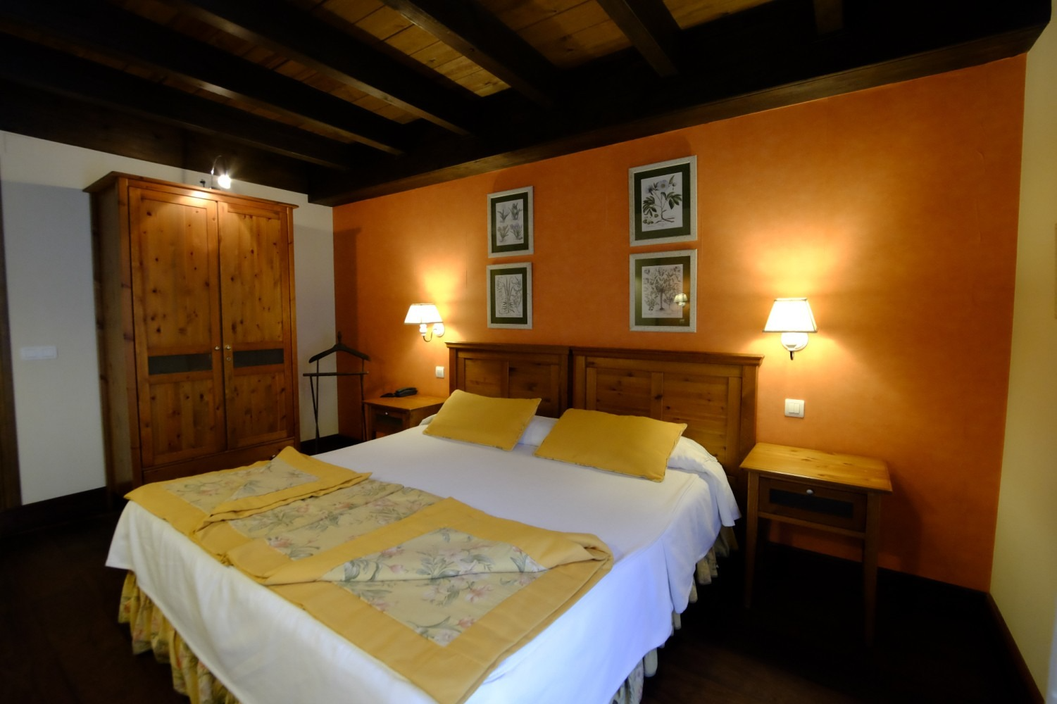 Dormitorio con muebles de madera, pared naranja, cama con detalles en amarillo, dos mesitas de noche y obras de arte.
