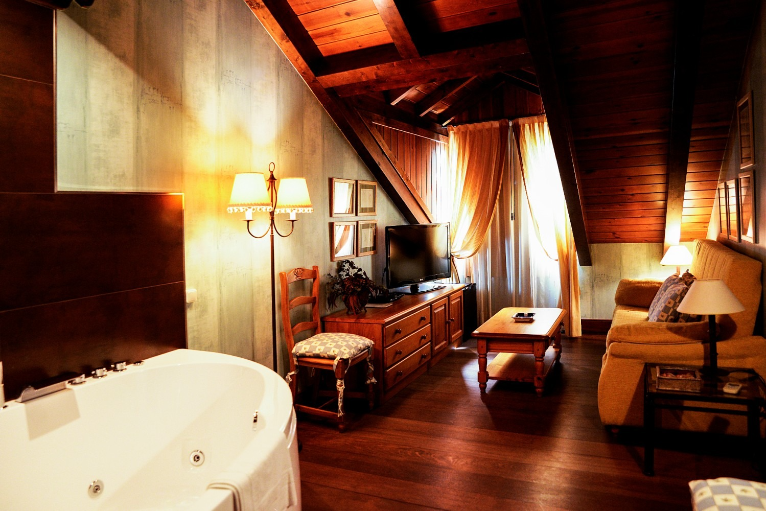 Acogedora habitación de hotel con jacuzzi, sofá, TV y techo de madera.