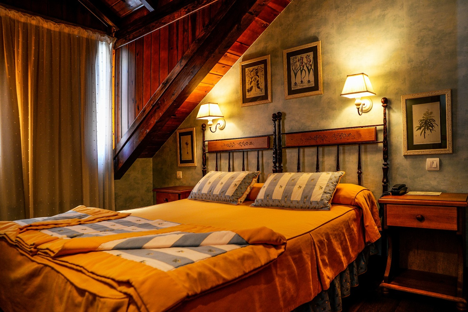 Dormitorio con vigas de madera, una cama con ropa de cama amarilla, dos mesitas de noche y apliques de pared.