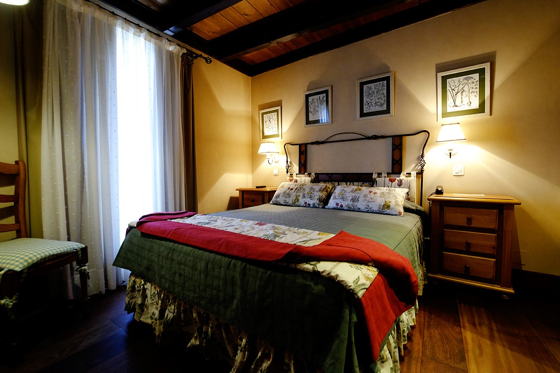 Dormitorio con techo de madera, pisos de madera y una cama con almohadas decorativas y una manta roja.